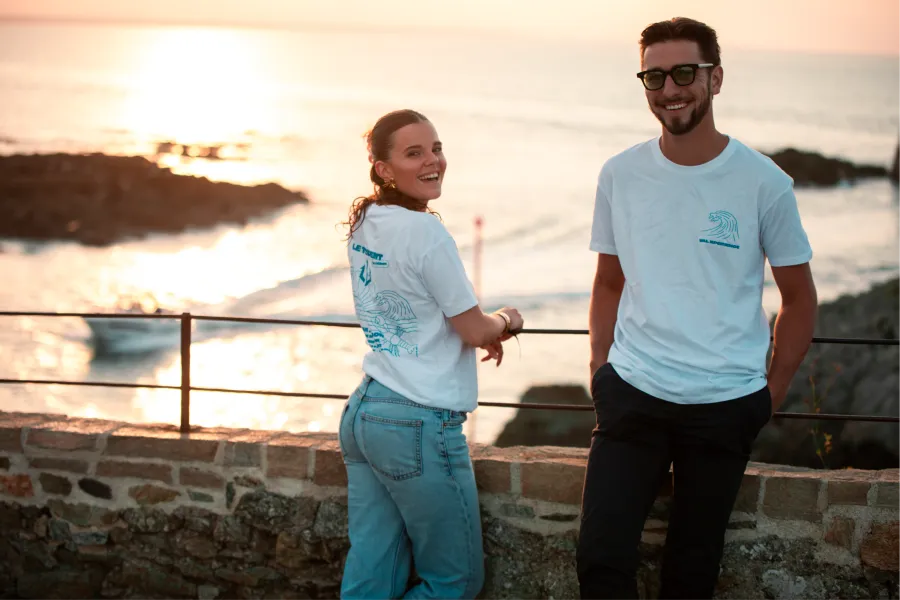 Deux membres de l'association en t-shirt du Trident Festival sur la digue de Pléneuf-Val-André, face à la mer, au coucher du soleil
